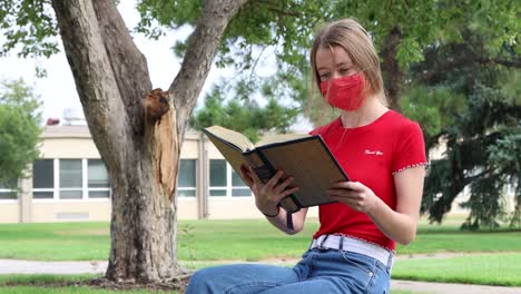 an american college student properly social distancing and wearing a mask while studying between classes