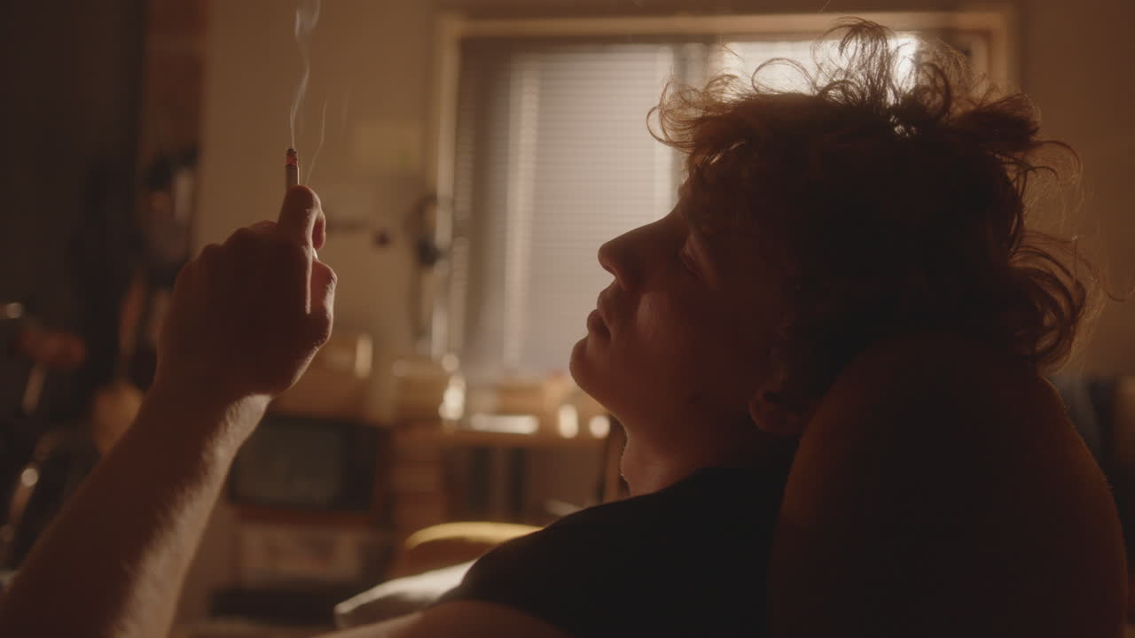 hombre melancólico sentado en casa, sintiendo anhelo y fumando un cigarrillo