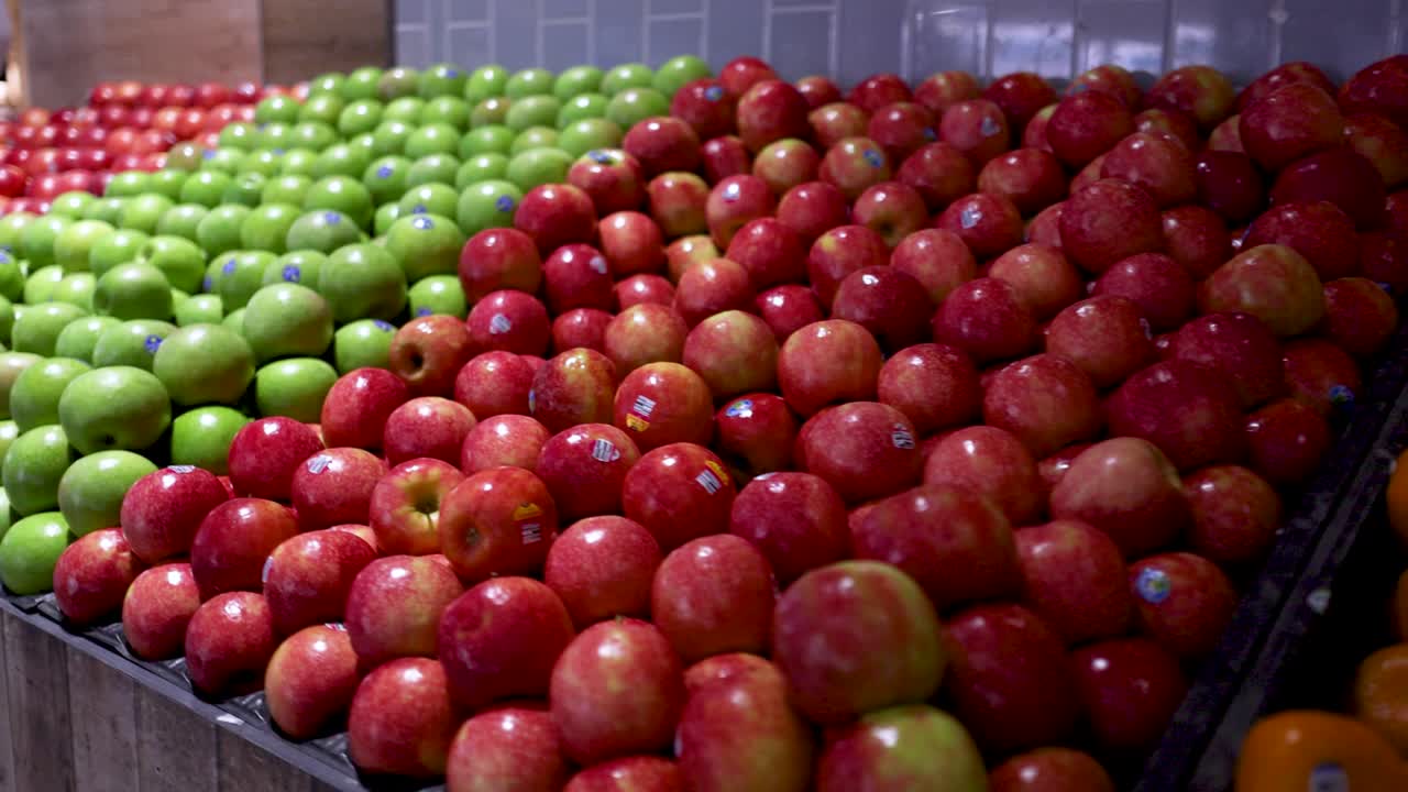 Rows of red and green apples neatly arranged in a well-lit supermarket setting, showcasing vibrant colors and symmetry