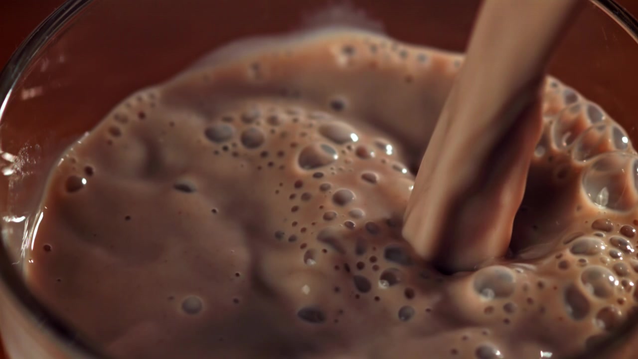 Delizioso latte al cioccolato che si versa in un bicchiere con bollicine