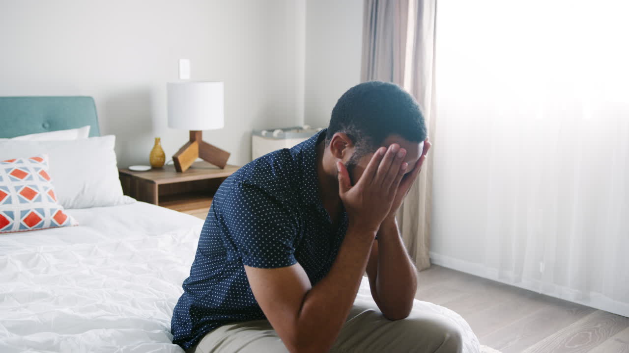 Giovane uomo che soffre di depressione seduto in camera da letto a casa.