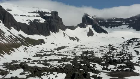 Grand-Drone-Aerial-Pullback-through-Amazing-Icelandic-snow-capped-grey-rock-cliffs-and-mountains-covered-in-clouds