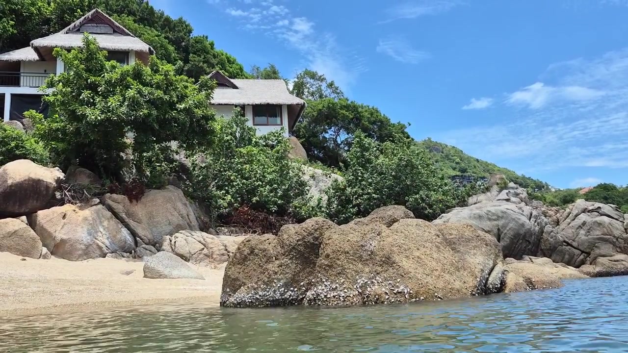 Large granite boulders and luxury resort villas nestled in lush green hillside on tropical beach in Koh Samui, Thailand