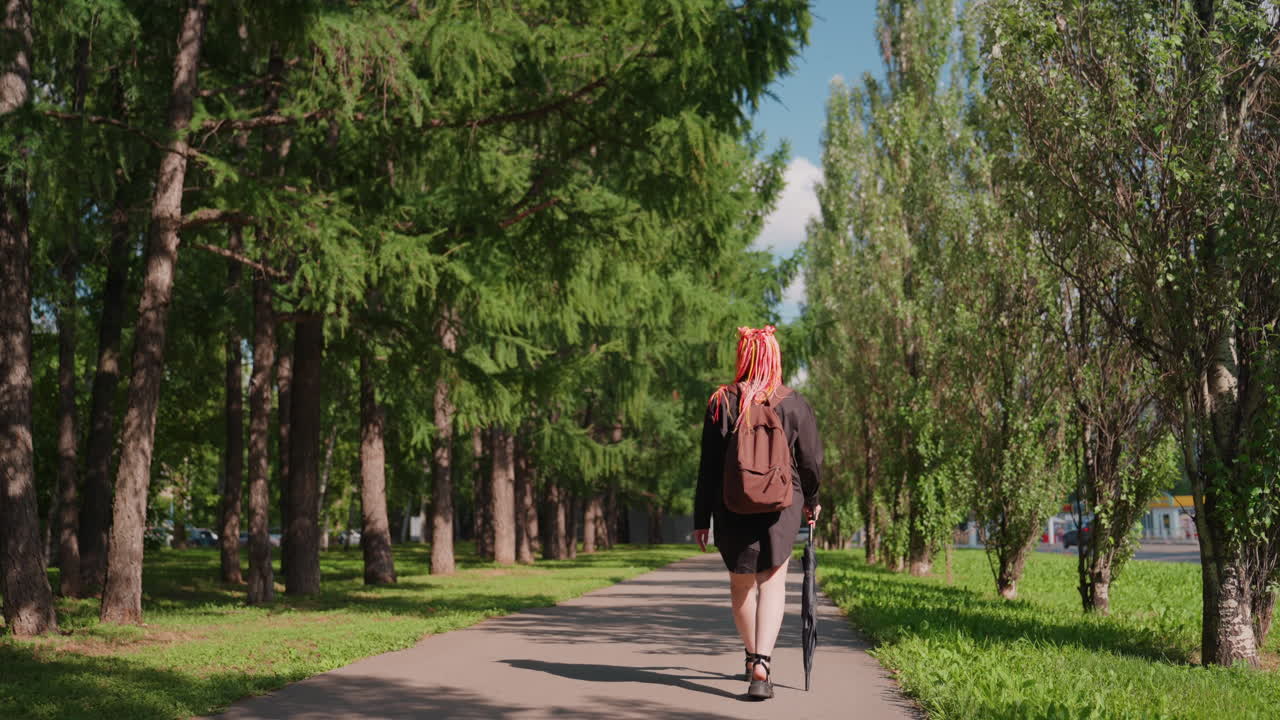 Una pelirroja dando un paseo tranquilo: una persona con rastas color carmesí camina por un sendero sombreado del bosque, una persona con rastas de fuego se mueve contemplativamente junto a un sendero arbolado salpicado de sol.