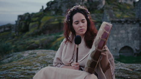 spiritual woman peacefully playing a shamanic drum in a beautiful medieval village medium shot