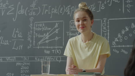 smiling young woman in a classroom with a blackboard full of scientific equations