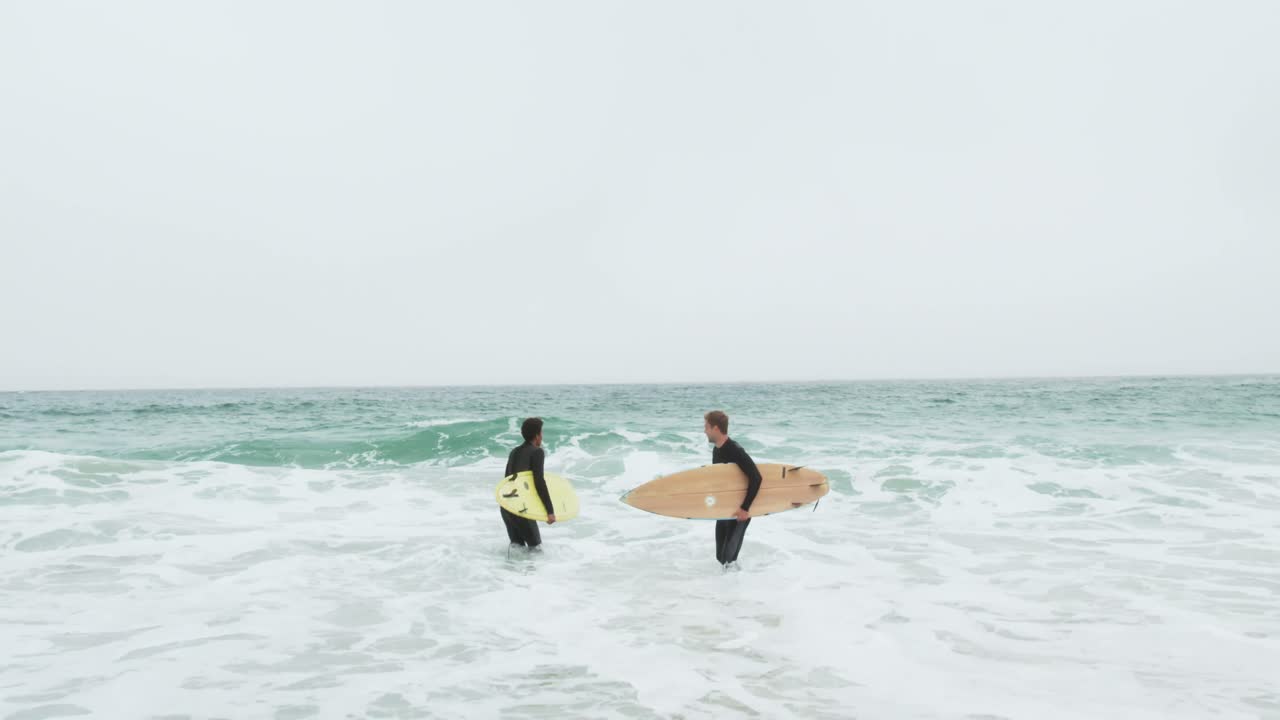 vista frontal de dos surfistas masculinos corriendo juntos con una tabla de surf en la playa 4k
