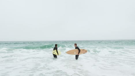 front view of two male surfer running together with surfboard on the beach 4k