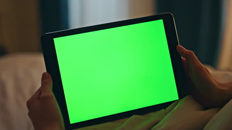 closeup tableta de pantalla verde en las manos en casa. persona de la noche ver chromakey en línea