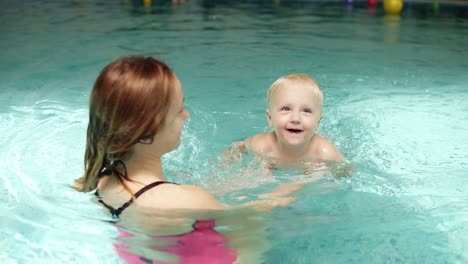 cute baby having swimming lesson with his mother. healthy family teaching their baby to swim in the swimming pool. young mother takes his son and embraces him while the kid is smiling