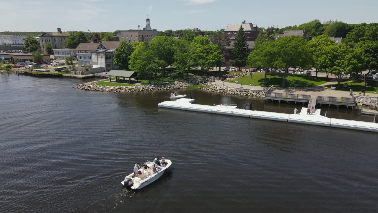 Aerial View of a Boat on a River Approaching Waterfront Docks and a Town