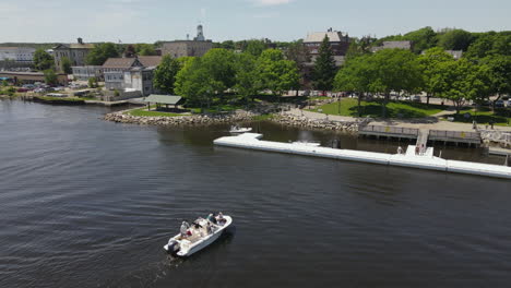 aerial view of a boat on a river approaching waterfront docks and a town
