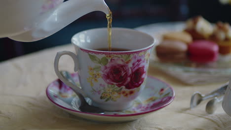 pouring tea into a cup with some light pastries and flower arrangements