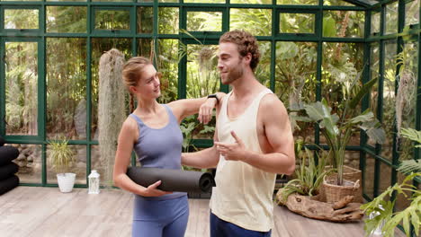 holding yoga mat, couple smiling and posing in glass house yoga studio