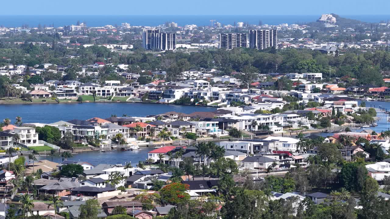 Sunny aerial panorama of waterfront residential neighborhood with lakes, greenery, and distant coastal skyline