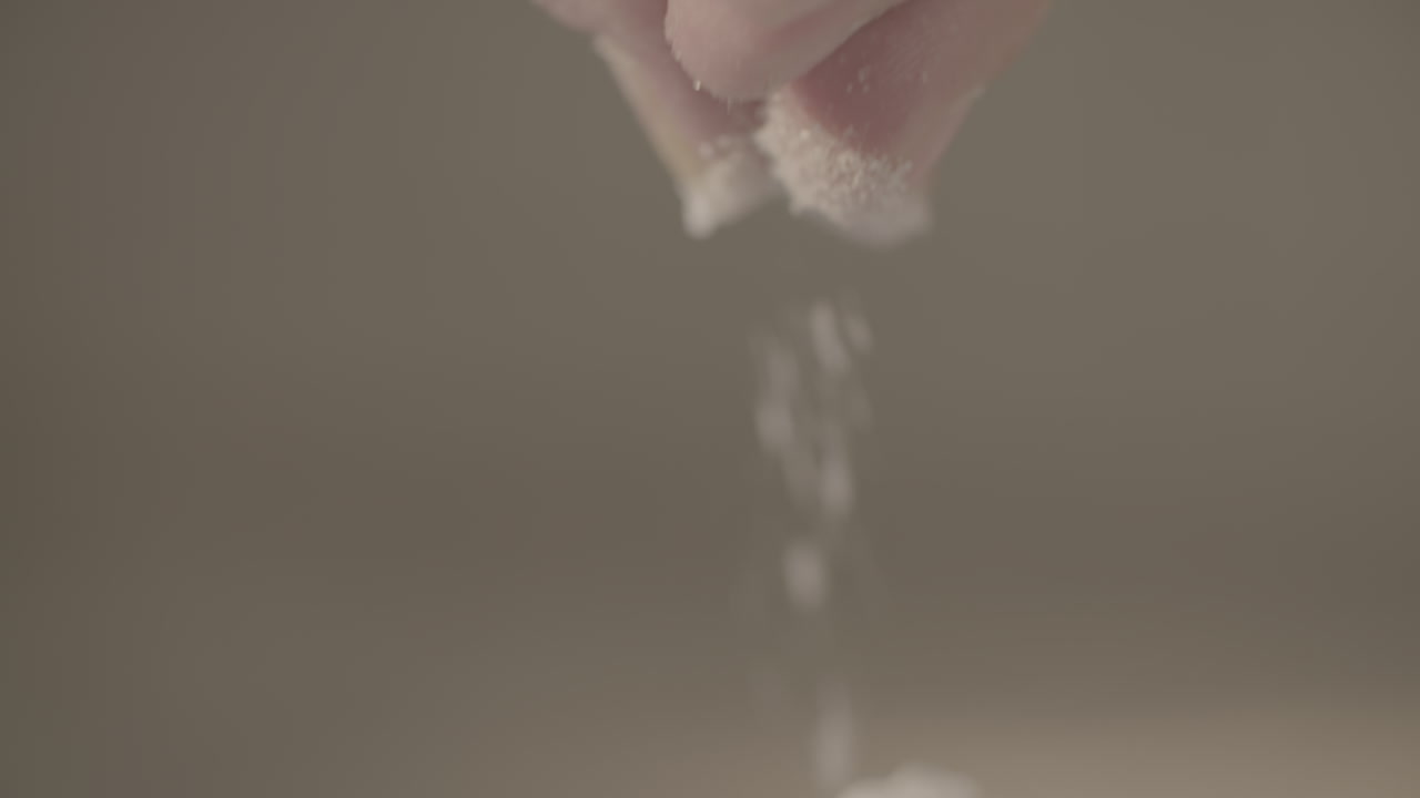 Close up slowmotion shot of a male hand dropping some salt on top of baking flour while moving his fingers LOG