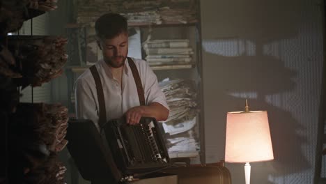 young male writer says goodbye to the past, moves, puts up his typewriter takes suitcases and goes to the library room at night