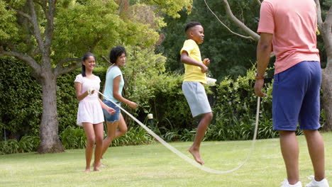 Felices-Padres-Afroamericanos,-Hijo-E-Hija-Saltando-En-Un-Jardín-Soleado,-Cámara-Lenta