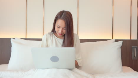 why work from home when you can work from anywhere, woman types on her laptop as she sits up in bed