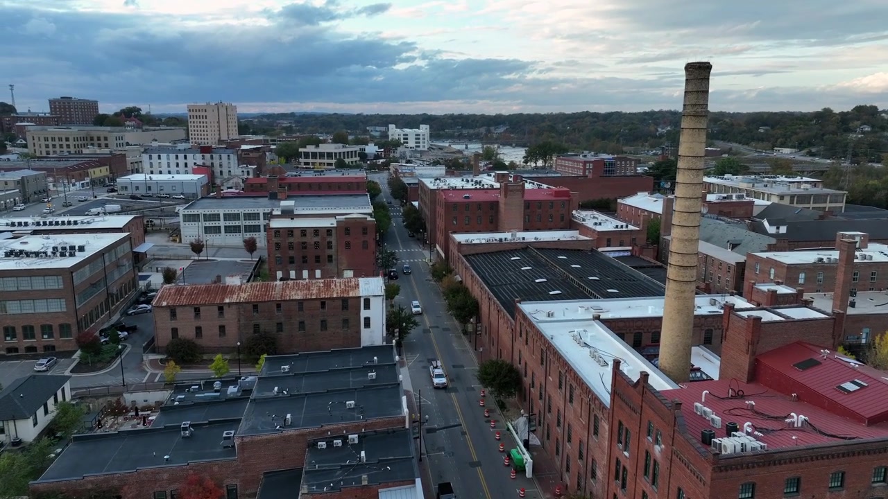 Ciminiera industriale nel centro di una città americana in una giornata nuvolosa. Auto che guidano su una strada tra case e appartamenti storici in stile mattone rosso. Danville, Virginia, USA. Volo aereo in avvicinamento.