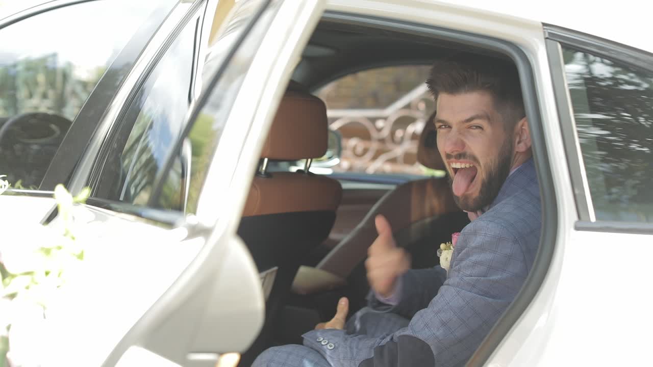 el novio se sienta en el coche. camiseta rosa y corbata de papagaio, chaqueta azul. sonrisa feliz. empresario