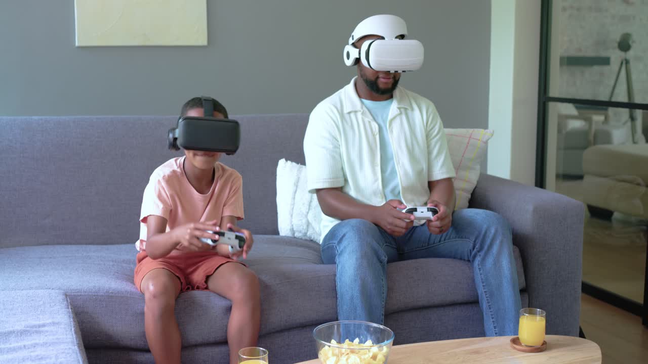 African American father and teen son playing VR game, pressing controller for fun on sofa headsets