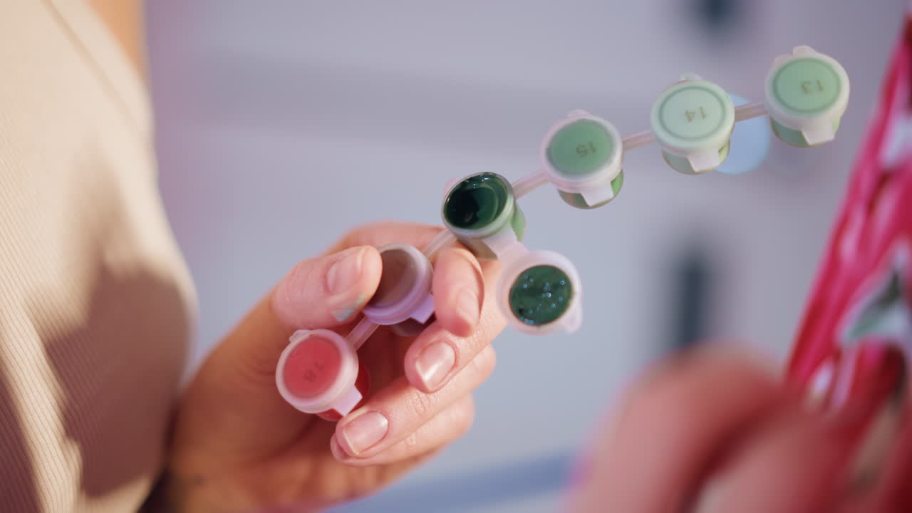 Close Action Of Brush Dipping Into Mini Pots And Applying Color To Floral Fabric, Caucasian Artist Balances Palette And Brush With Focused Motion, Bright Studio Light Accentuates Pigment And Texture