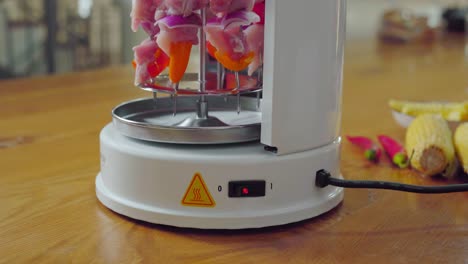 female hand clicking on button for electric shish kabob grill with skewers