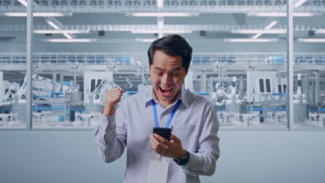 asian male professional worker standing with his smartphone at factory digitalization, he raises his fist up with screaming goal