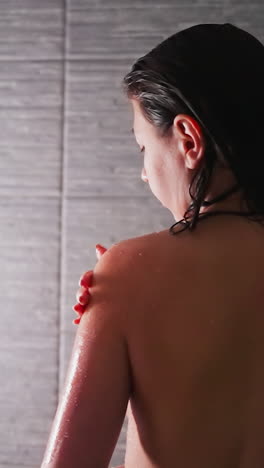 woman takes care of skin with scrub in shower cabin closeup. graceful lady applies peeling natural cosmetic product on shoulder in bathroom