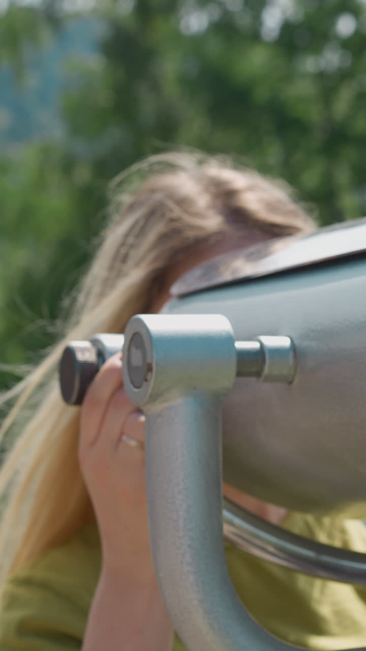 poderoso dispositivo de binoculares turísticos se encuentra en la cubierta de observación y la dama con el cabello largo agitado por el viento mira a través de los árboles en un día soleado en cámara lenta