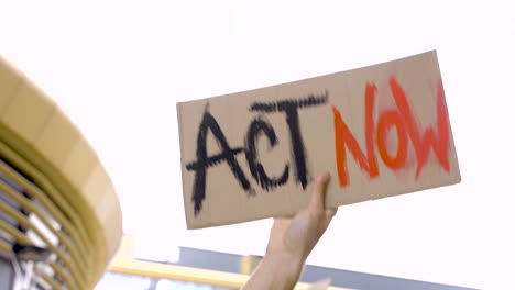 jovem com boné preto segurando cartaz com mensagem de ato agora em um protesto