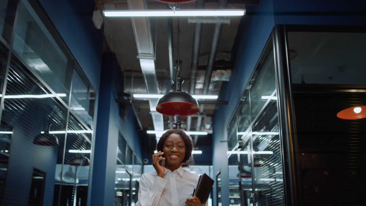 Donna afro allegra che usa il telefono nel corridoio. Donna che parla al telefono in ufficio.