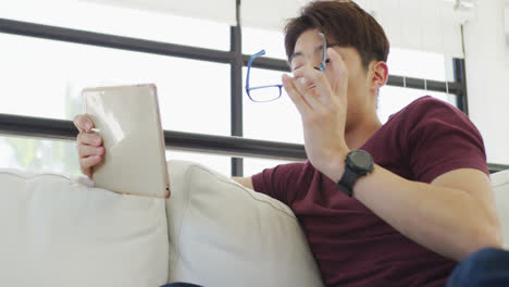 asian male teenager wearing glasses and using tablet in living room