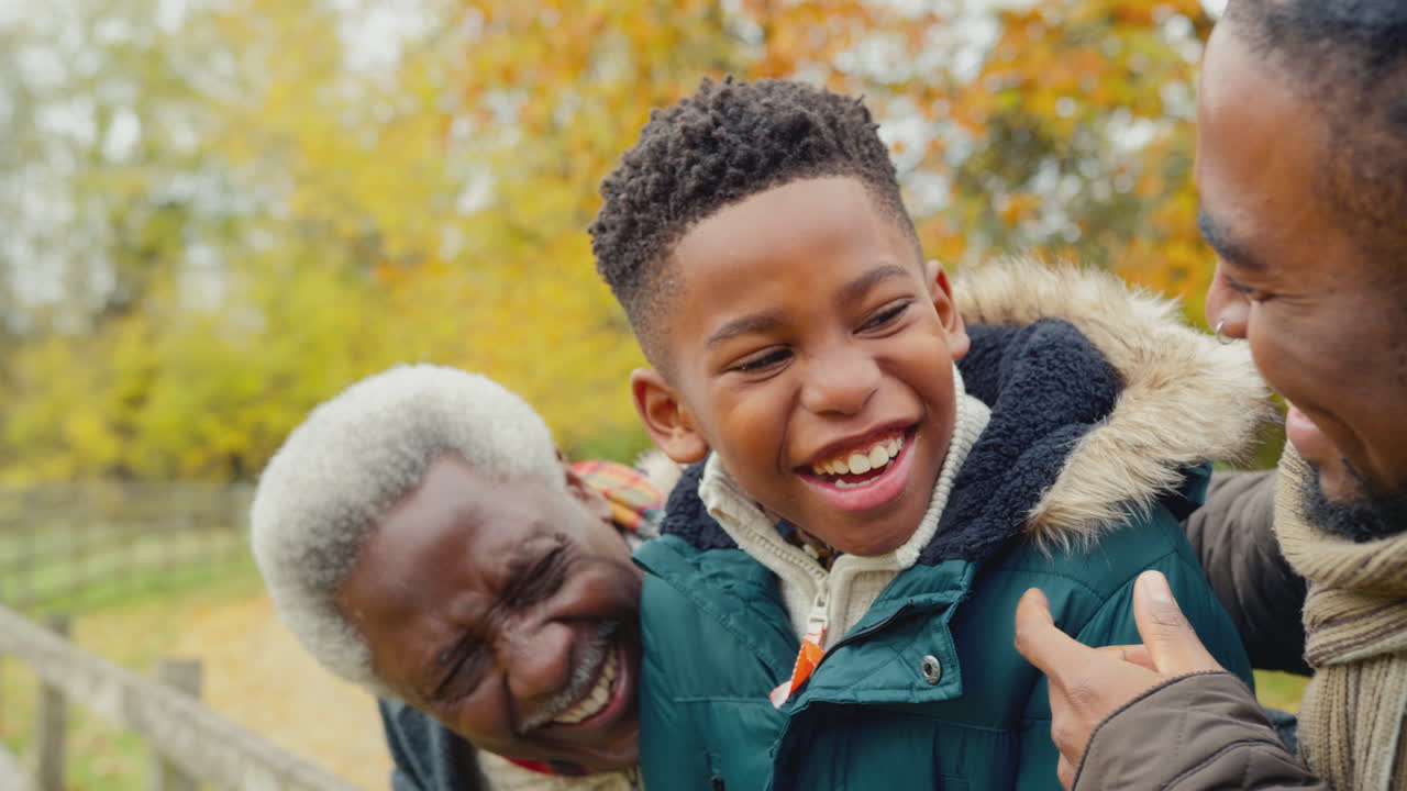 Portræt af mandlig familie i flere generationer, der står ved en låge på tur gennem efterårslandskabet - filmet i slowmotion