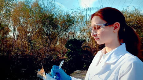 una joven científica en un arroyo, con gafas de protección y una bata de laboratorio, tomando notas en un clipboard