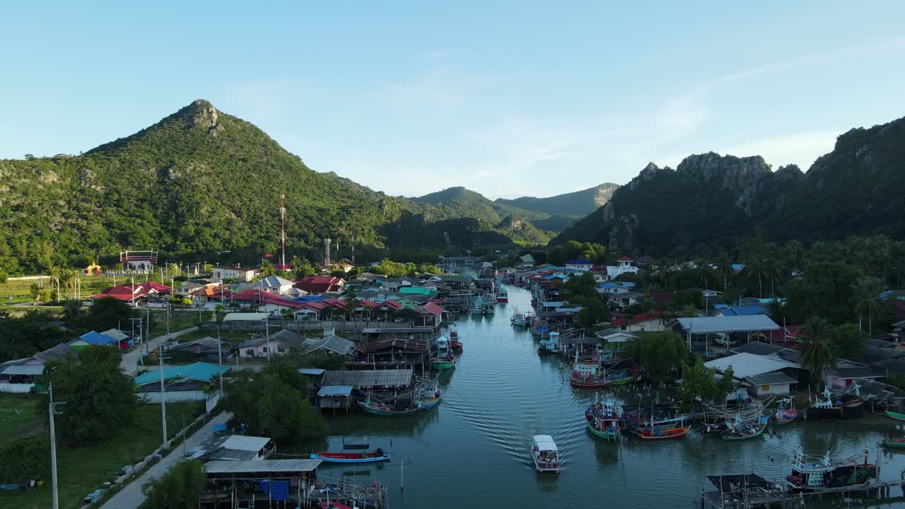 Cảnh quay từ trên không hướng về làng chài, hé lộ một chiếc thuyền đang di chuyển, nhiều thuyền neo đậu và phong cảnh tuyệt đẹp.