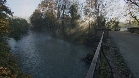 the first sun shine through the trees on the river lambro in italy during a cold morning in autumn