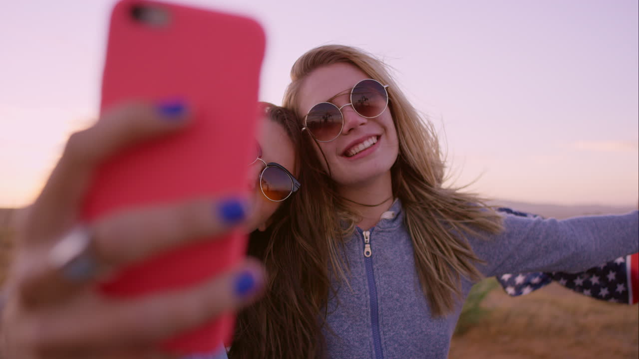 Belle amiche che si scattano selfie durante un viaggio on the road al tramonto con un'auto d'epoca