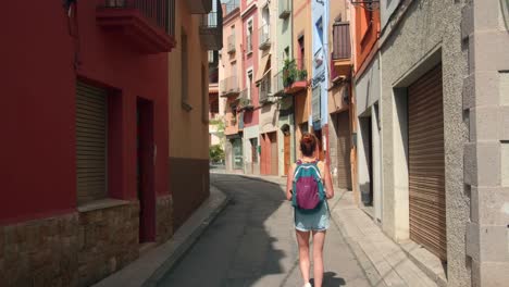 back view of beautiful tourist woman walking around castelló d'empúries historic center in costa brava, spain - wide, static shot