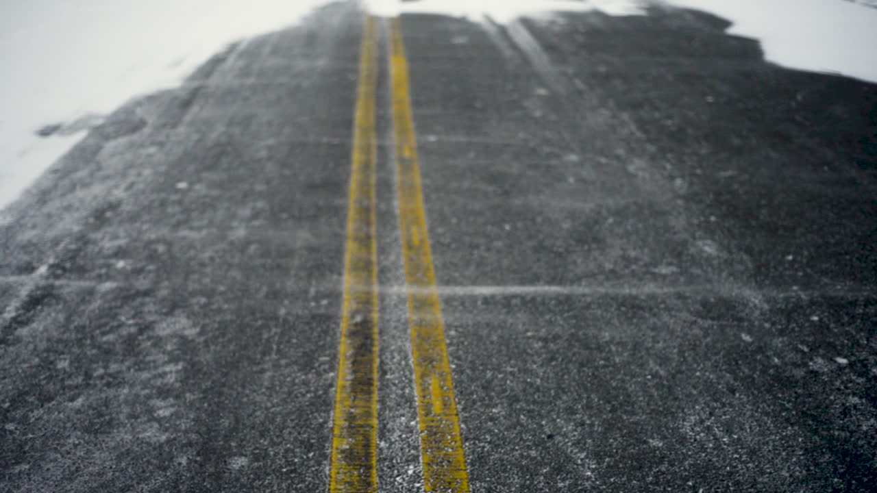 Snow blows across and empty road on a cold winter day.
