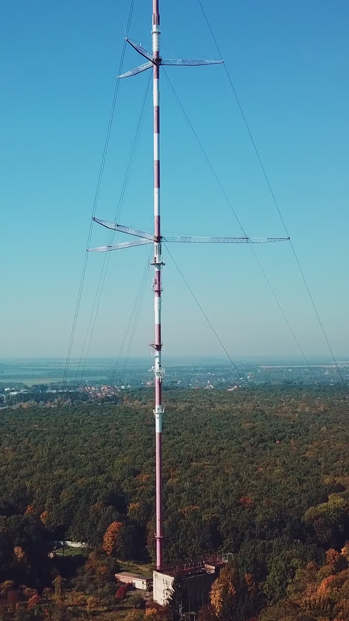 high telecommunication antenna on the background of forest and cityscape. Camera motion up Vertical video