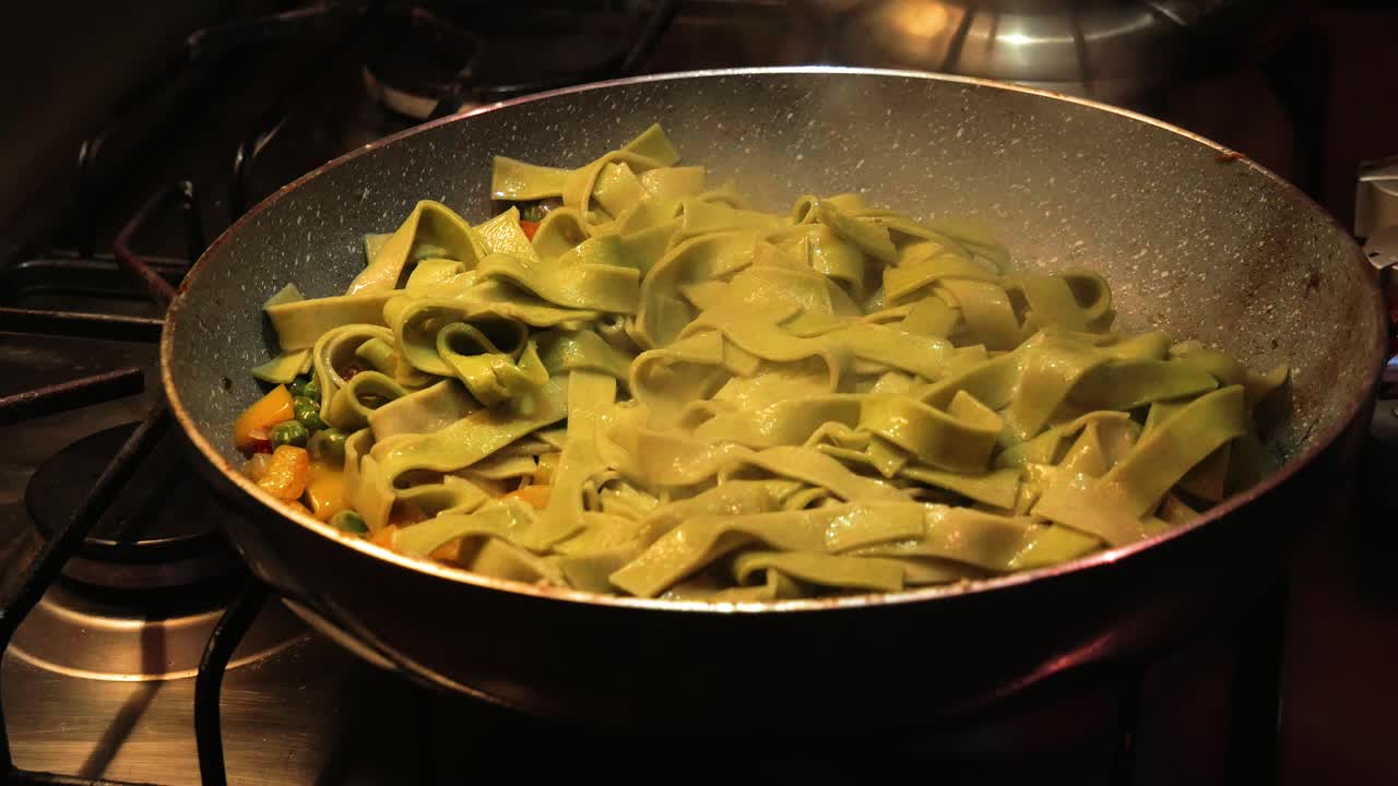 Adding cooked green spinach egg pasta on the top of vegetable garnish in hot pan while frying