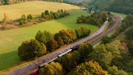 steam train with passenger cars driving through an autumn landscape on a sunny day