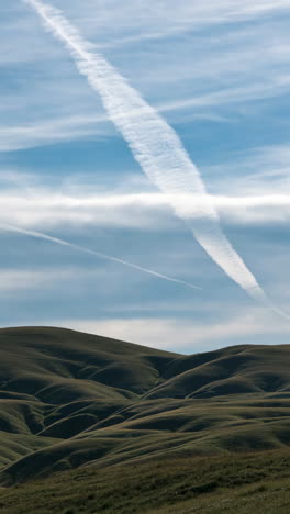sky with contrails over hills