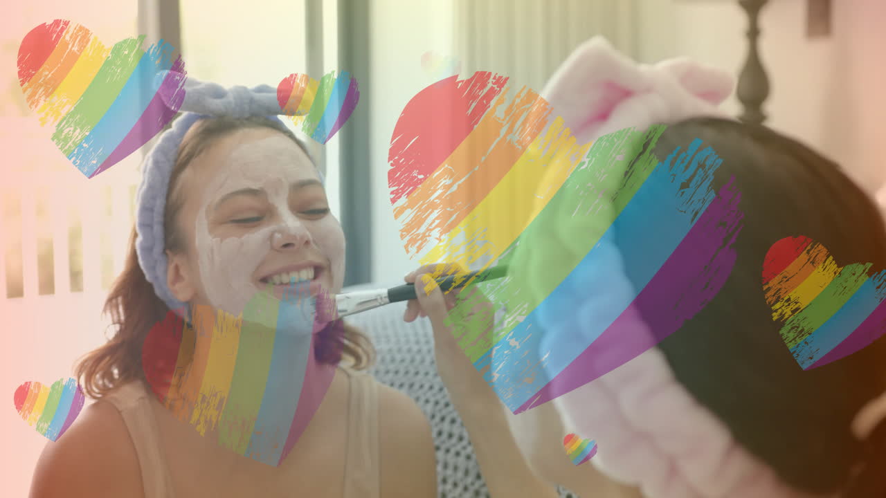 aplicando máscara facial, dos mujeres disfrutando de la rutina de cuidado de la piel con animación de corazones arco iris