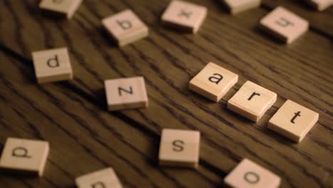 wooden scrabble-style tiles spell out art as the camera pans across a rustic wooden surface in warm lighting.