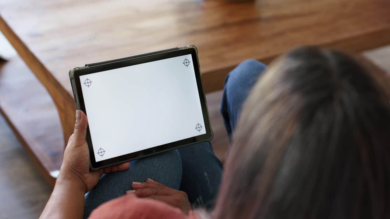 Senior woman is noticing corner alignment marks, adjusting tablet on lap to align screen near bench