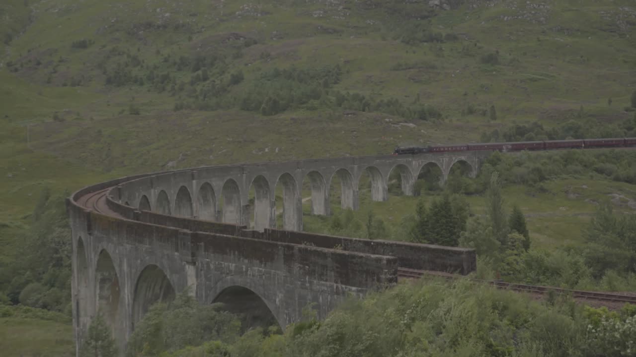 Famous steam train crossing a curve arched stone bridge in a beautiful landscape in scotland uk. Green landscape and white smoke