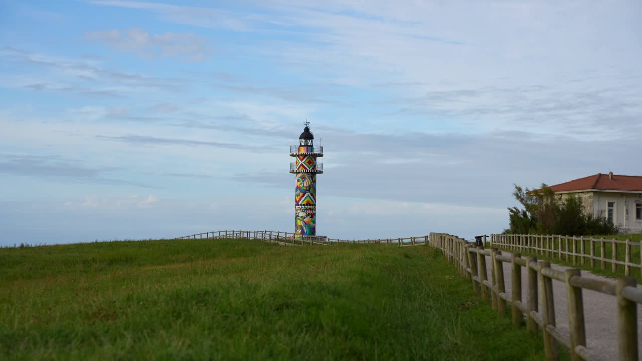 Colorful lighthouse in Ajo, Cantabria with vibrant geometric art by Okuda San Miguel on a windy day